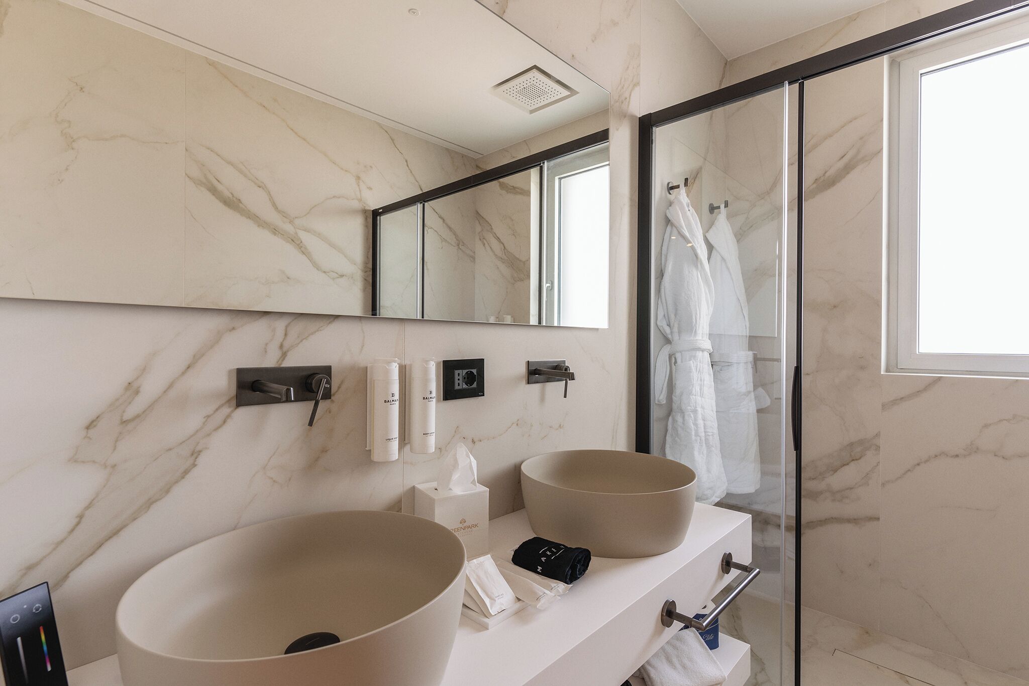 Une salle de bain moderne avec deux grands lavabos, une douche à l’italienne en verre et un grand miroir.