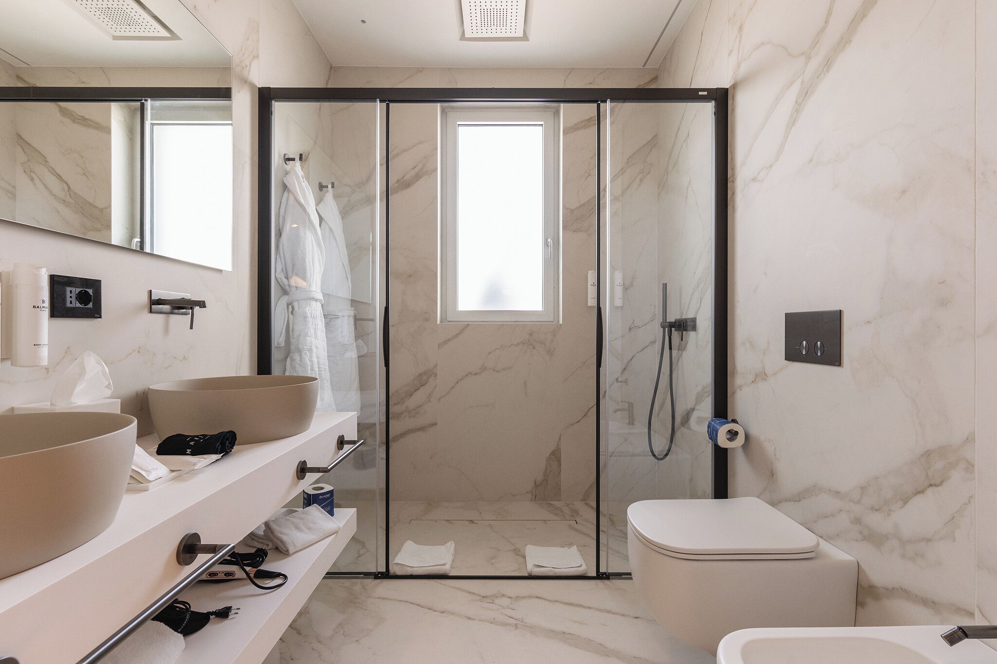 A modern bathroom with a large mirror, two sinks, a shower enclosure, and a toilet.