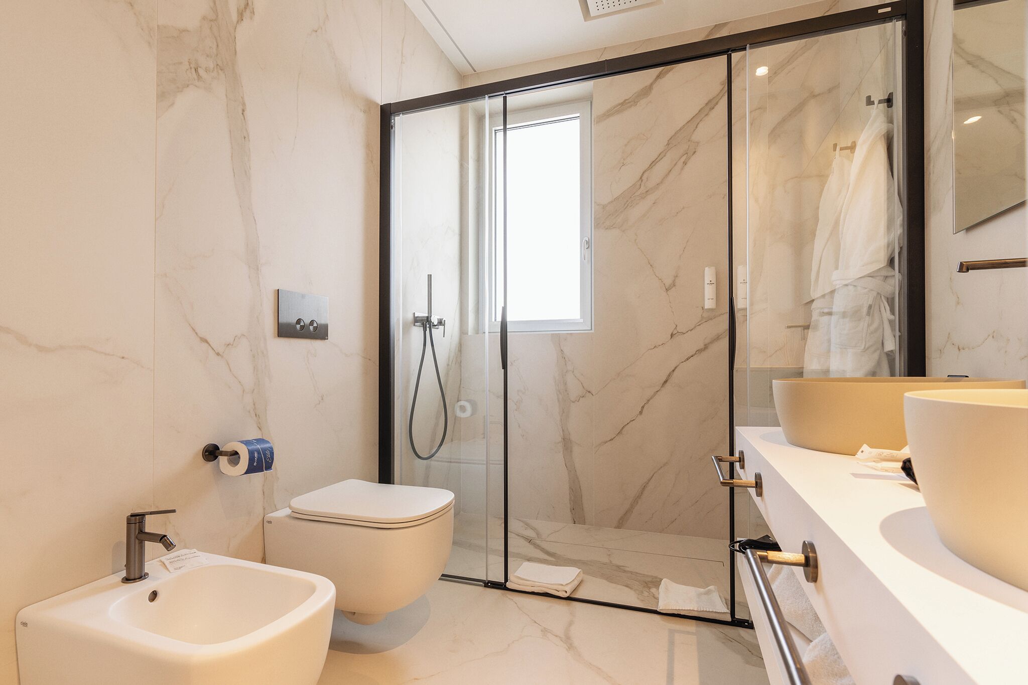 A modern bathroom with a glass-enclosed shower, a bidet, a toilet, and a vanity with two sinks.