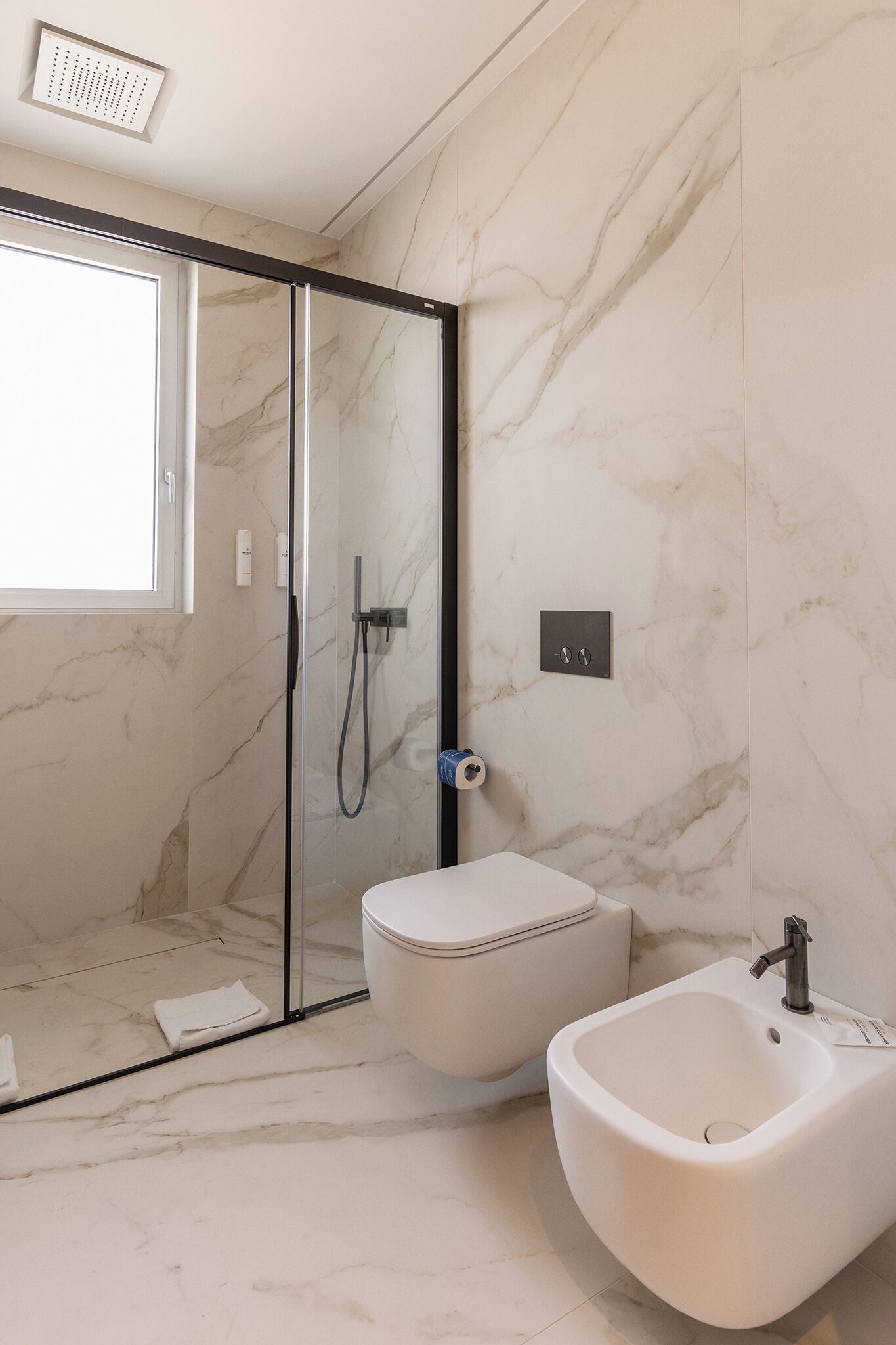 Ein modernes Badezimmer mit einer ein Glasfachwerk-Duschkabine, einem Bidet und Marmorwänden.