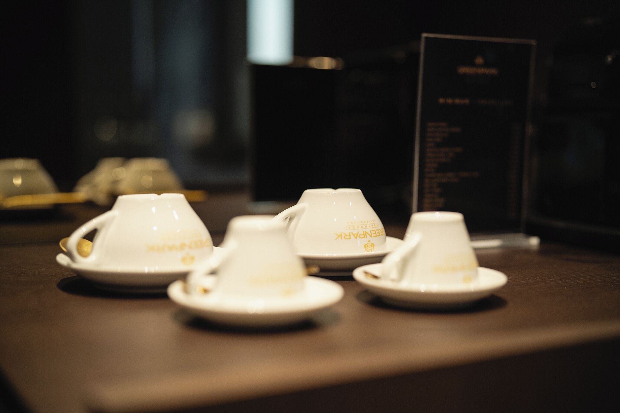 A table with four white cups and saucers, each with a logo, and a menu stand in the background.
