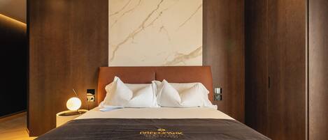 A hotel room with a large bed, a marble wall, wooden paneling, and a nightstand with a lamp.