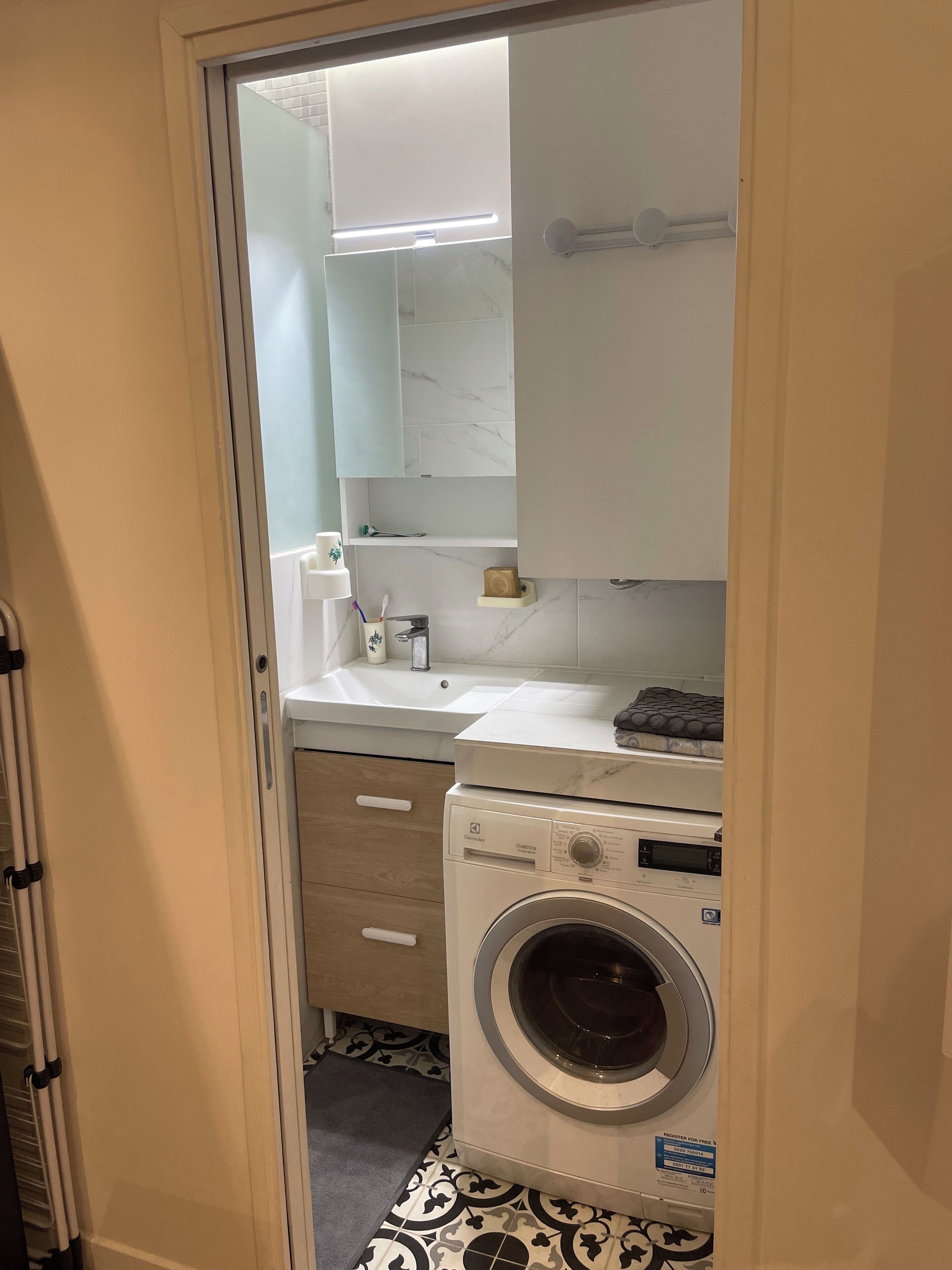 A compact laundry room with a washing machine, a sink, and a mirror.