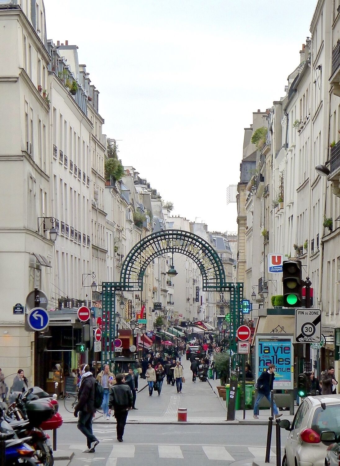A busy urban street with pedestrians, traffic signs, and a green archway.