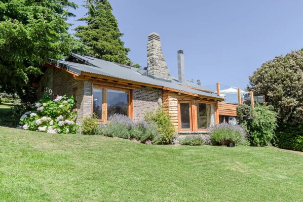 A log cabin with a stone chimney, large windows, and a well-maintained garden.