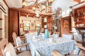 A dining area with a long table set for four, wooden chairs, and a rustic chandelier.