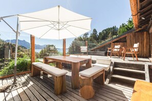 An outdoor wooden deck with a table and benches, an umbrella, and a view of mountains and trees.