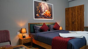 A hotel room with a bed, a wooden wardrobe, a nightstand with a lamp, a chair, and a table with a book and a glass of water. -  SG Boutique Stay (Near Railway Station) (Udaipur)
