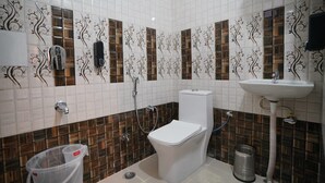 A bathroom with white tiled walls, a toilet, a sink, and a shower. -  SG Boutique Stay (Near Railway Station) (Udaipur)