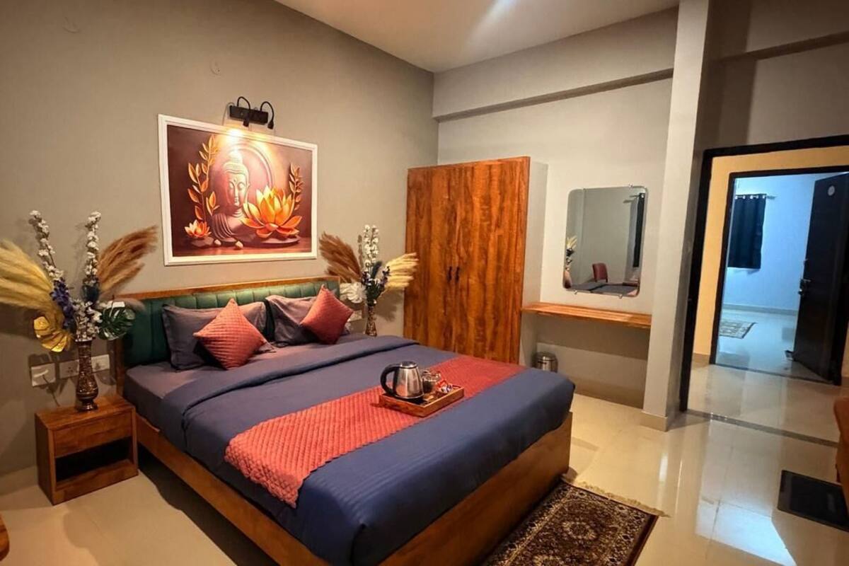 A modern bedroom with a large bed, a wooden wardrobe, a bedside table with a lamp, and a framed picture on the wall.