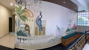 A hotel lobby with a mural of peacocks and tropical plants, a staircase, and a view of the outdoors through a window. -  SG Boutique Stay (Near Railway Station) (Udaipur)