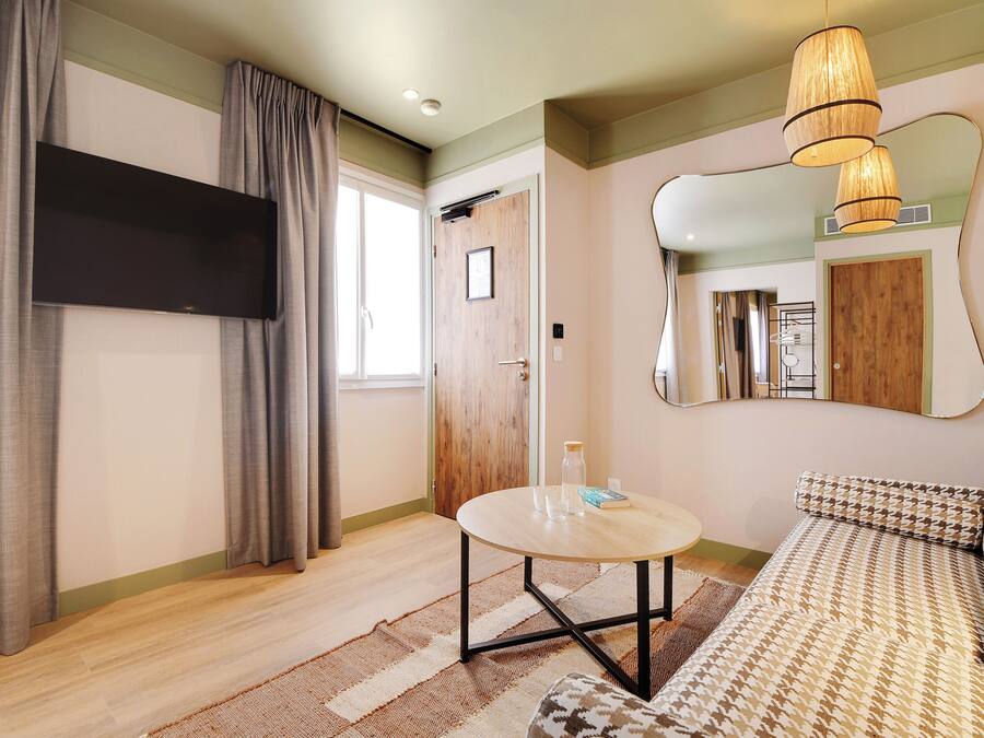 A room with a sofa, a round table, a flat-screen TV, and a mirror on the wall.