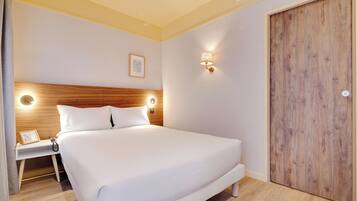 Un lit bien fait, avec du linge de lit blanc, une tête de lit en bois, des lampes de chevet et une porte en bois.