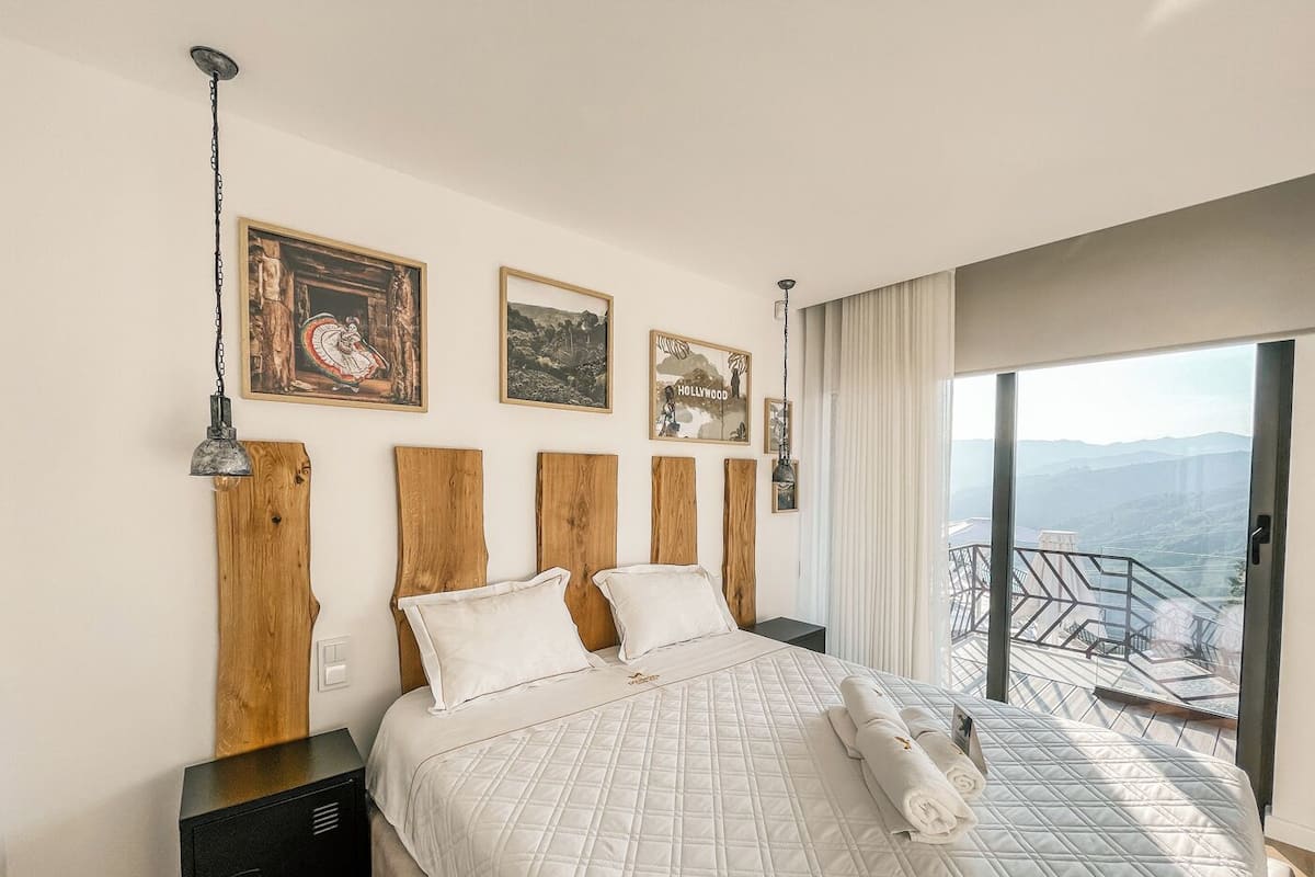 Une chambre dotée d’un grand lit, d’une tête de lit en bois et offrant une vue sur les montagnes depuis un balcon.
