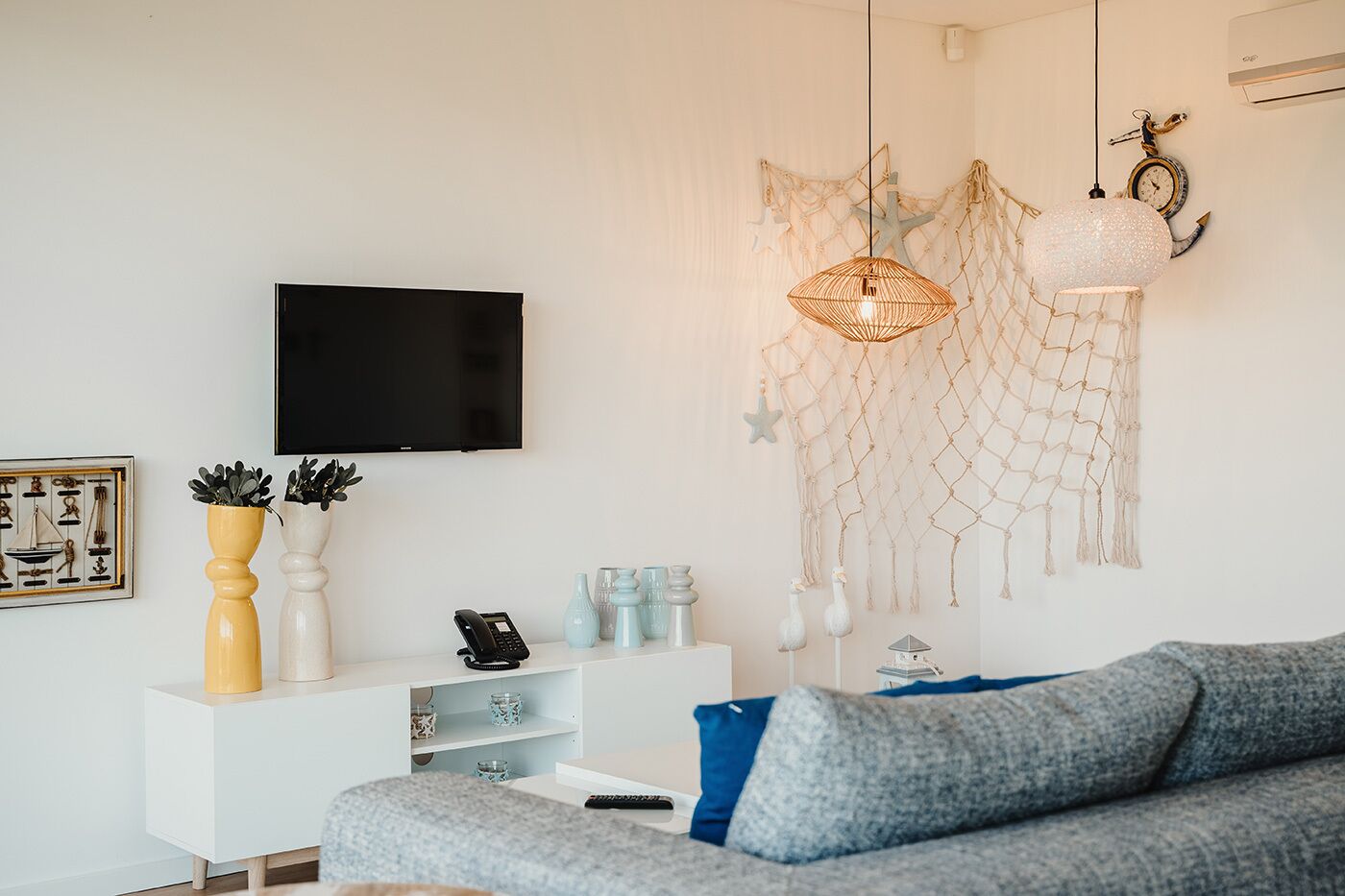 Ein modernes Wohnzimmer mit einem grauen Sofa, einer weißen TV-Konsole und einer dekorativen Pendelleuchte.