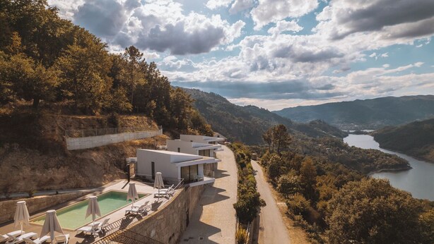 A modern hotel with a pool, overlooking a valley and a lake.