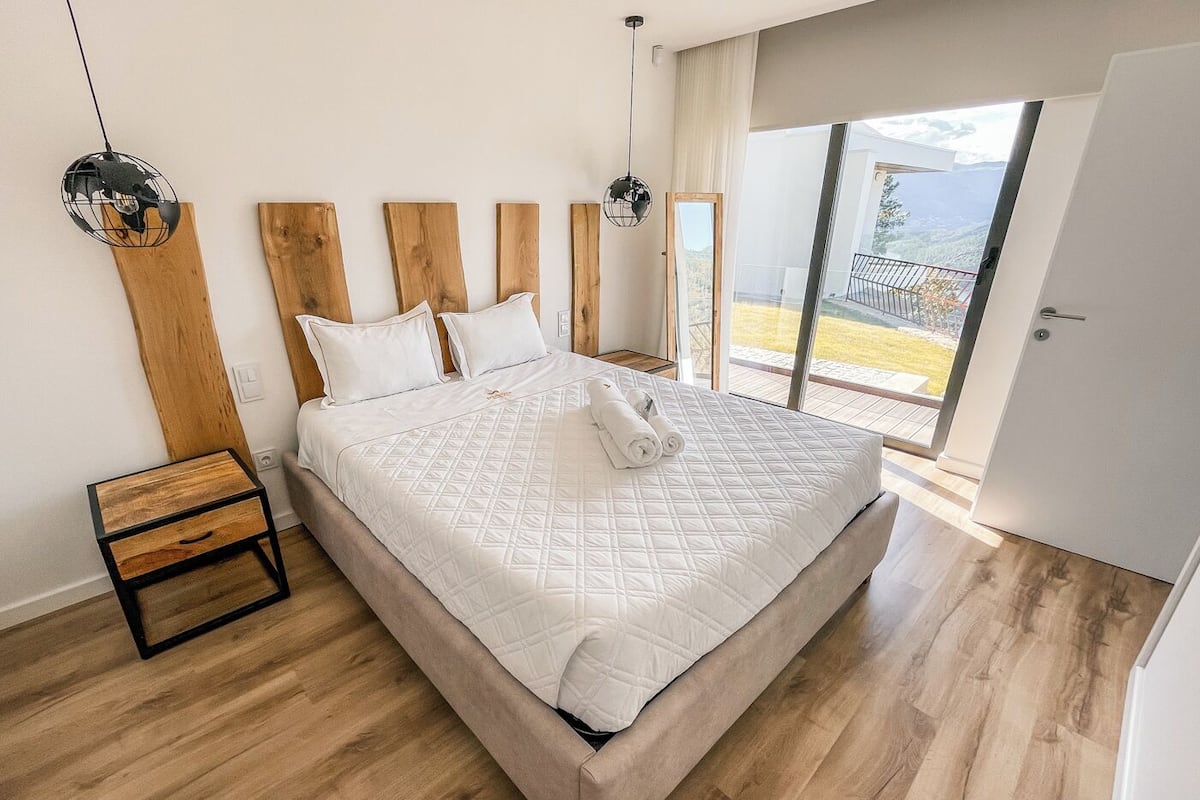 Une chambre moderne avec un grand lit, une tête de lit en bois et une vue sur un balcon.
