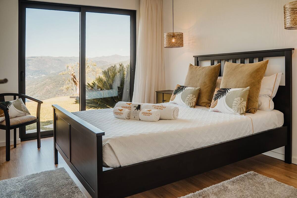 Une chambre avec un grand lit, une chaise, une table de chevet et une vue sur l’extérieur.