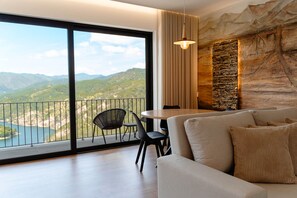 A modern living room with a large balcony, a stone wall, and a view of mountains. - Encosta de Louredo by Pousadela Village (Vieira do Minho)
