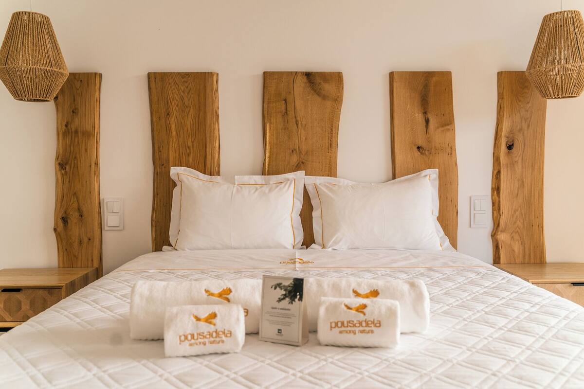 Une chambre d’hôtel avec un grand lit, une tête de lit en bois, du linge de lit blanc et deux tables de chevet avec des lampes.