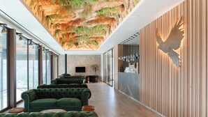 A modern interior with a green upholstered sofa, a wooden reception desk, and a wall-mounted bird sculpture.