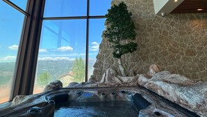 A hot tub with a rocky backdrop and a view of the mountains through large windows.