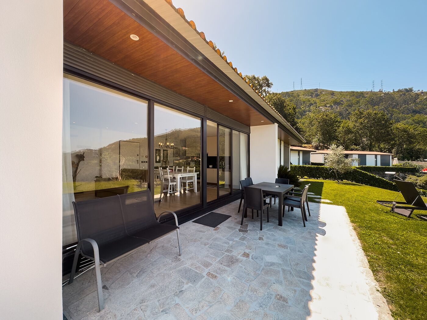 A modern patio with a dining area, large glass windows, and a view of the surrounding landscape.