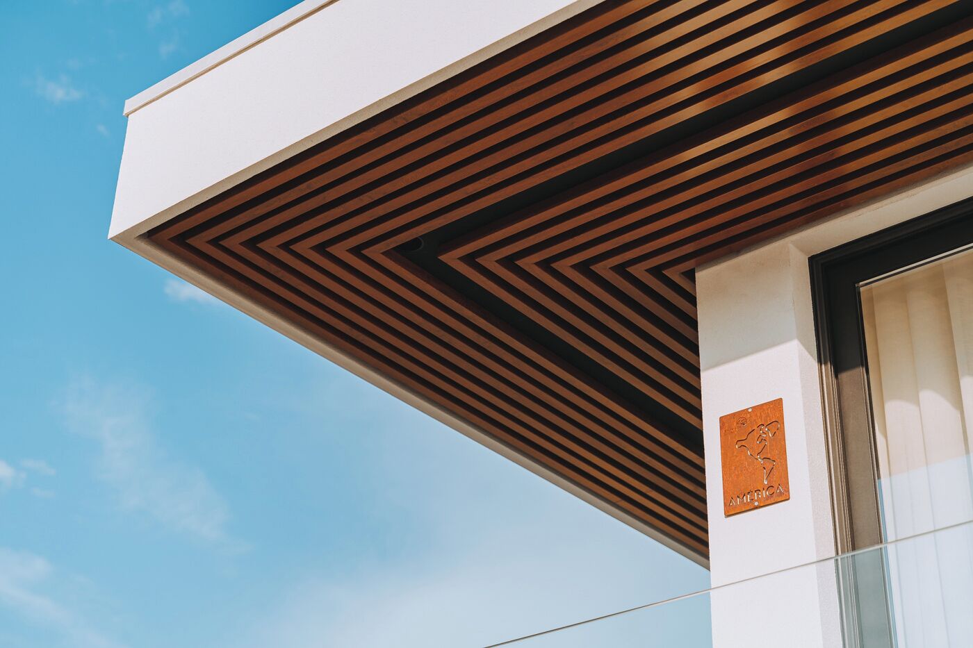 Un edificio moderno con un diseño geométrico de listones de madera en la fachada y un cielo azul claro al fondo.