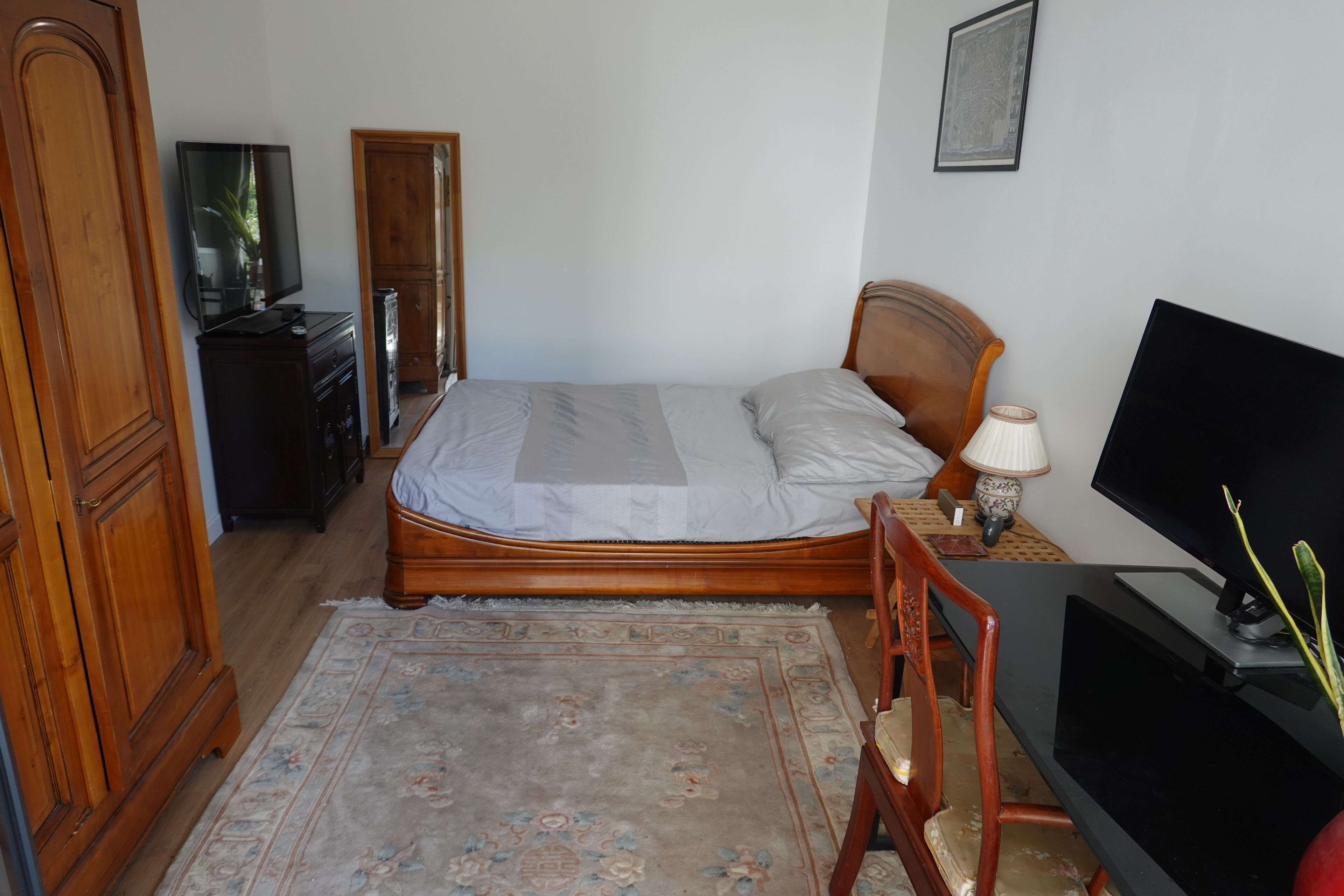 Une chambre à coucher comprenant un lit, une armoire en bois, une télévision et un bureau avec une lampe.
