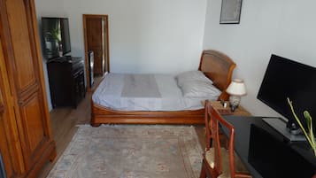 Een slaapkamer met een bed, een houten kledingkast, een televisie en een bureau met een lamp.
