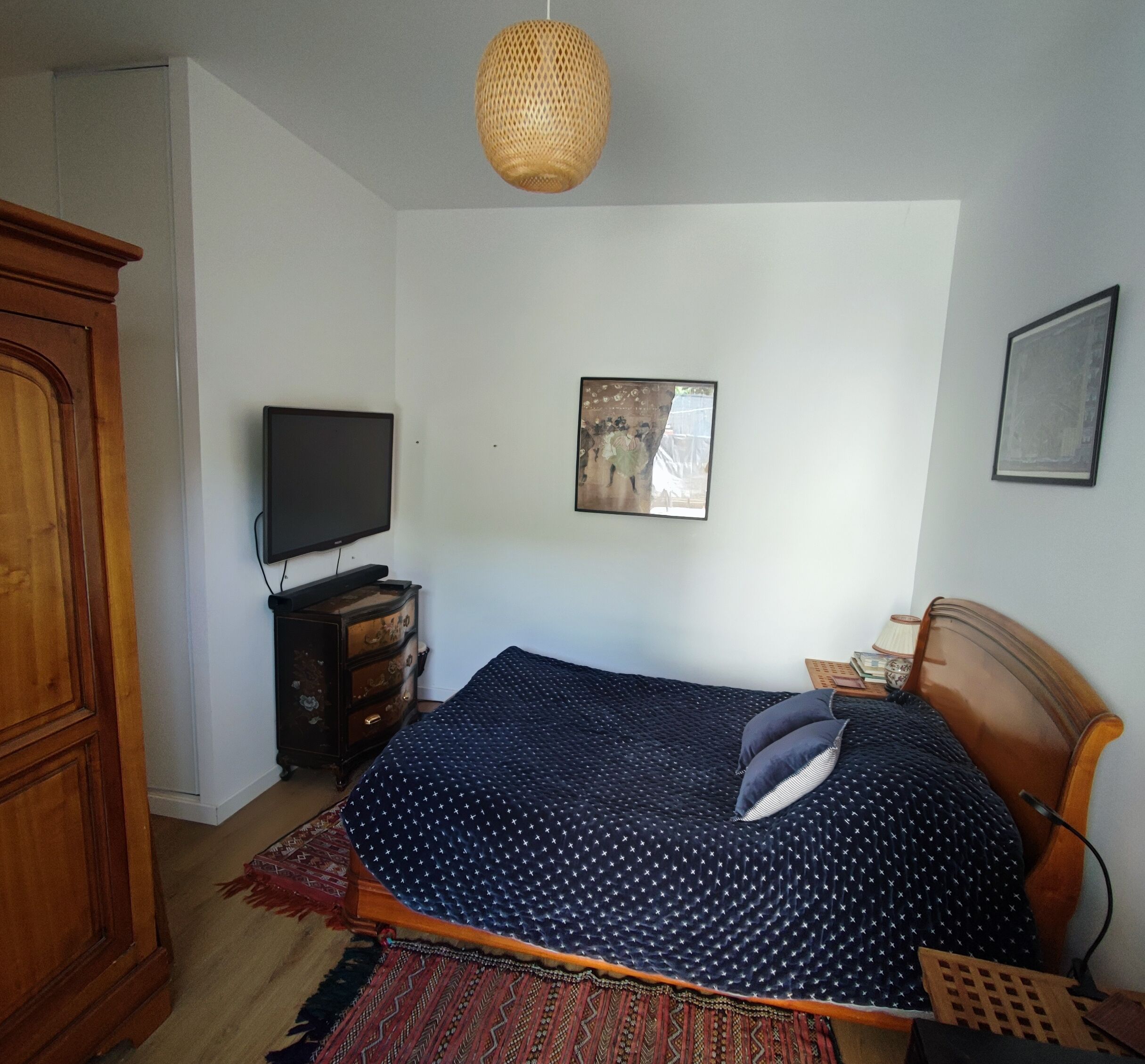 Een slaapkamer met een bed, een televisie, een dressoir en een hanglamp.