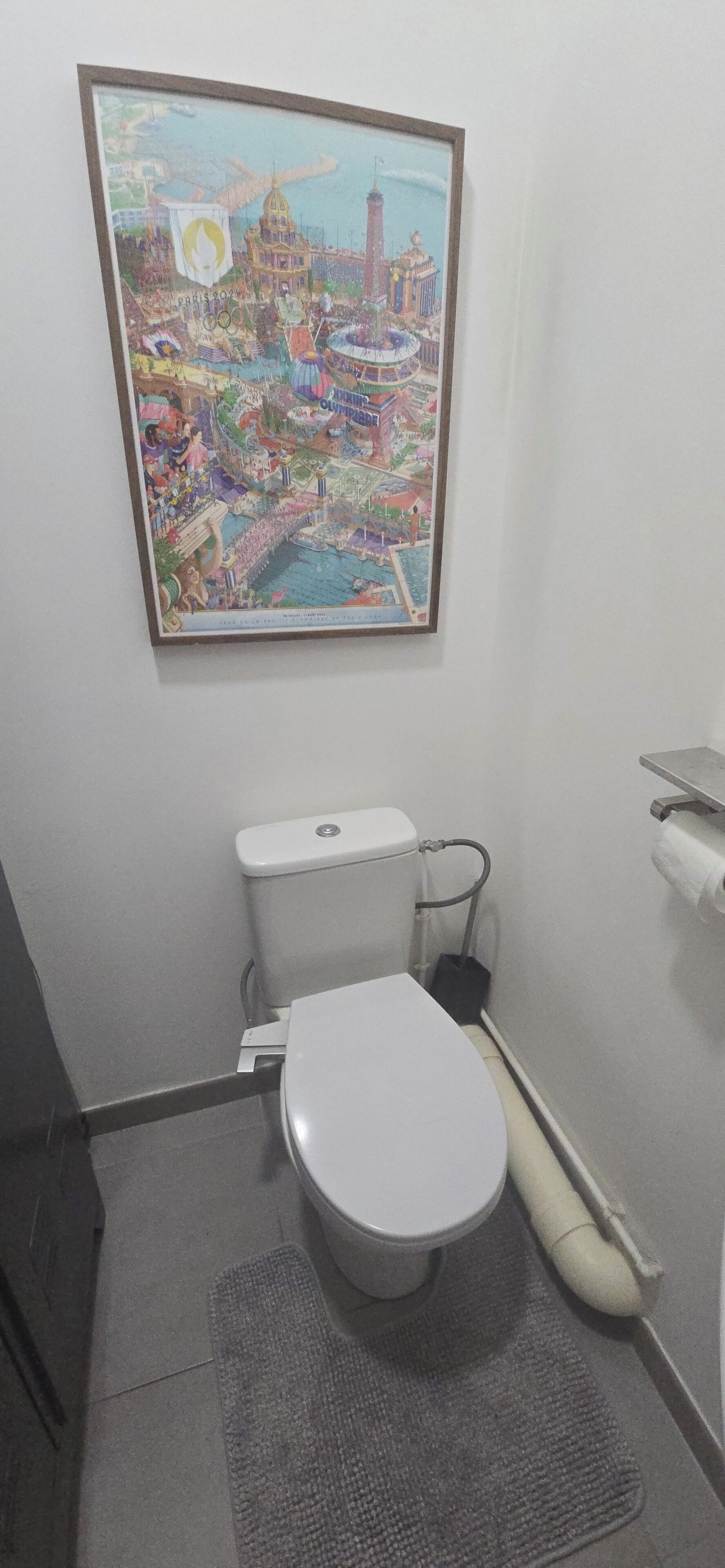 Une petite salle de bain comprenant des toilettes, un bidet, un porte-rouleau de papier toilette et un tableau représentant une vue de la ville, accroché au mur.
