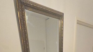 Une console en bois foncé, sur laquelle repose un bol, avec un miroir au-dessus et un thermostat fixé au mur, à gauche.