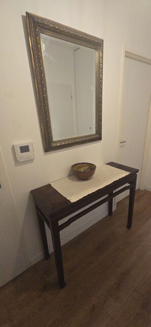 A dark wooden console table with a bowl on top, a mirror above it, and a thermostat on the wall to the left. - Large room near metros 7 and 14 (Le Kremlin-Bicêtre)