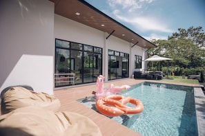 A modern house with a swimming pool, outdoor furniture, and a large window overlooking the backyard. - Issara Private Pool Villa Khaoyai A (Pak Chong)