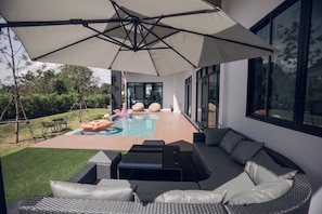 A modern outdoor living area with a pool, outdoor furniture, and a large umbrella. - Issara Private Pool Villa Khaoyai A (Pak Chong)