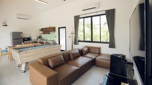 A modern living room with a pool table, a sofa, a television, and a kitchen area in the background. - Issara Private Pool Villa Khaoyai A (Pak Chong)