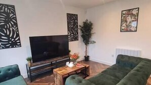 A living room with a flat-screen TV, a wooden coffee table, a green sofa, and a potted plant. - Welcome to our centrally-located 4-bedroom detached new build home in Stafford (Stafford)