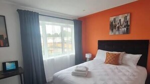 A hotel room with a large bed, a nightstand, a desk, and a window with curtains. - Welcome to our centrally-located 4-bedroom detached new build home in Stafford (Stafford)