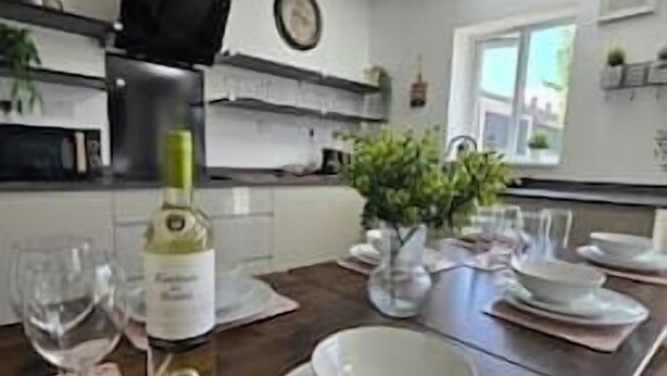 A dining area with a wooden table set for a meal, a bottle of wine, and a clock on the wall. - Welcome to our centrally-located 4-bedroom detached new build home in Stafford (Stafford)