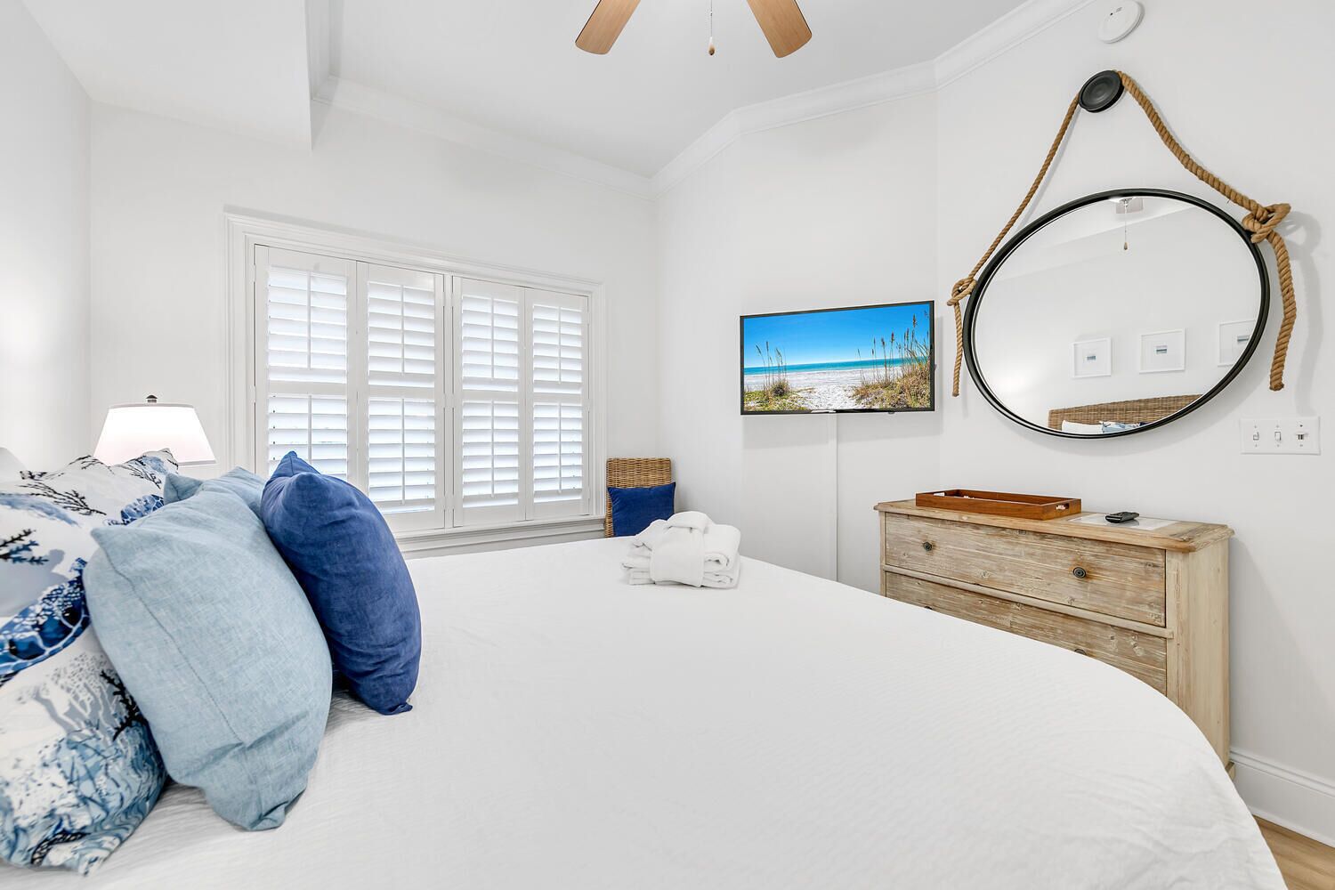 Een slaapkamer met een bed, een dressoir, een spiegel en een raam met jaloezieën.