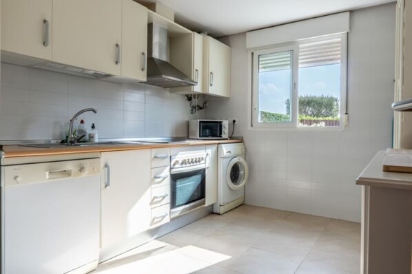 A compact kitchen with a dishwasher, washing machine, microwave, and a window with a view. - Casa Viv - Beautiful Spacious 2 bed apartment in the lovely La Torre Golf Resort (Torre-Pacheco)