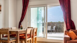 A dining area with a wooden table and chairs, a sofa, and a sliding glass door leading to an outdoor patio. - Casa Viv - Beautiful Spacious 2 bed apartment in the lovely La Torre Golf Resort (Torre-Pacheco)