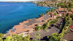 A coastal hotel with solar panels on the roof, a parking lot, and a view of the ocean.