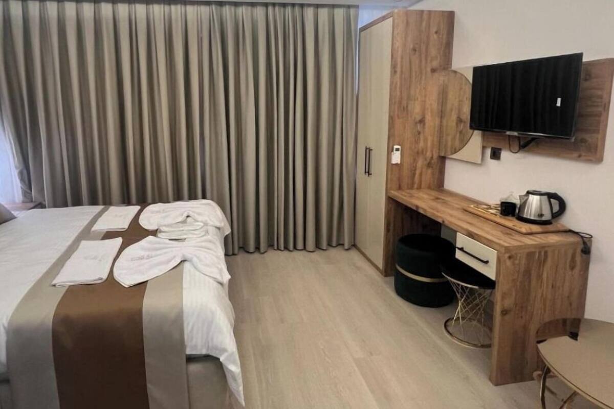 A hotel room with a bed, a wooden desk, a television, and a small table.