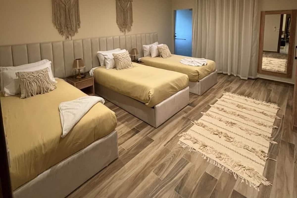 A modern hotel room with three beds, a large mirror, and a wooden floor.