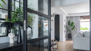 Ein modernes Wohnzimmer mit einem grauen Sofa, einem schwarzen Konsolentisch mit Dekoration und einem großen Fenster mit Blick auf Grünfläche.