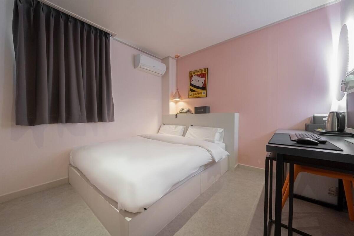 Quarto de hotel com uma cama, uma mesa, ar-condicionado e um cartaz na parede.
