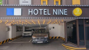 A hotel entrance with a sign reading 'HOTEL NINE,' a parking area with two cars, and a '9 HOTEL' sign above the entrance. - Hotel Nine (Uiwang)