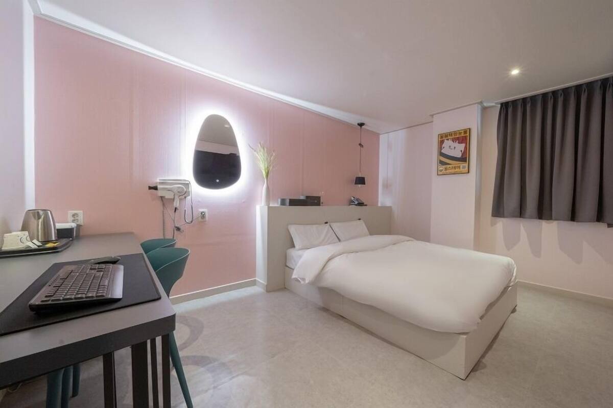 Quarto de hotel com cama, escrivaninha, laptop, secador de cabelo e espelho.